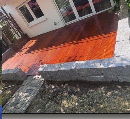 Frisch geölte Holzterrasse mit sauber eingefasster Natursteinmauer und Pflasterung